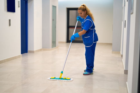 Une agente de nettoyage professionnelle en uniforme nettoyant un sol dans un bâtiment de bureaux à Marseille.